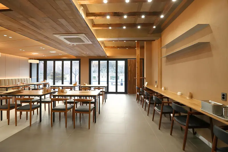 울산 식당인테리어 시공사례 — 옥국밥 울산 남구, 목재 천장 아래 테이블석과 벽면 바 좌석을 둔 홀